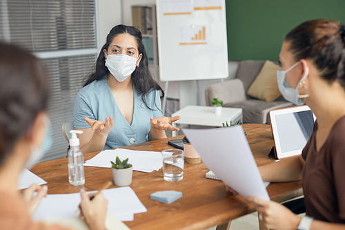 Portrait of businesswoman wearing mask while tlking to female colleagues in brainstorming meeting