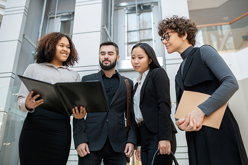 Smiling Afro-American manager holding open folder while presenting project plan to colleagues