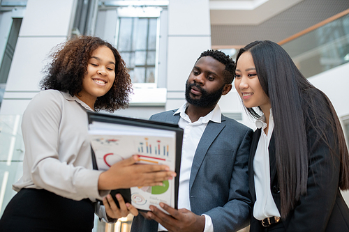 Smiling friendly Black financial consultant assisting young business couple with budget analysis