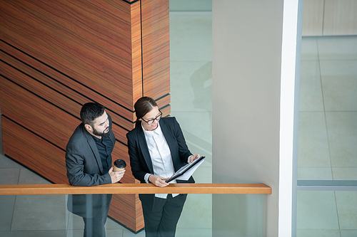 Above view of young woman in glasses standing on balcony and presenting sales data in papers to manager