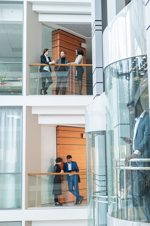 Young office employee standing on balconies and discussing work in modern financial district