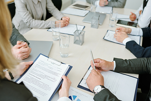 Hands of young elegant business partners discussing text of contract or preparing reports for conference at meeting in boardroom