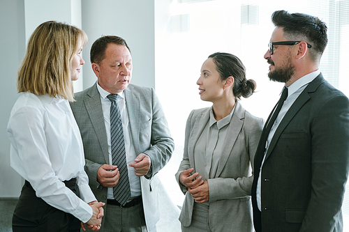 Three subordinates in formalwear listening to their mature mixed-race employer during consultation about forthcoming revision