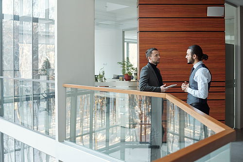 Two young contemporary elegant businessmen discussing terms of new deal at meeting inside large business center