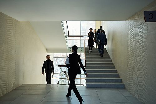 Several young intercultural people in formalwear moving upstairs and forward inside large contemporary business center