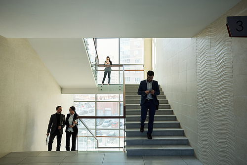 Contemporary young elegant office workers in formalwear going downstairs and upstairs while communicating