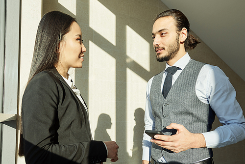 Two young intercultural colleagues in formalwear discussing points of their report before business conference