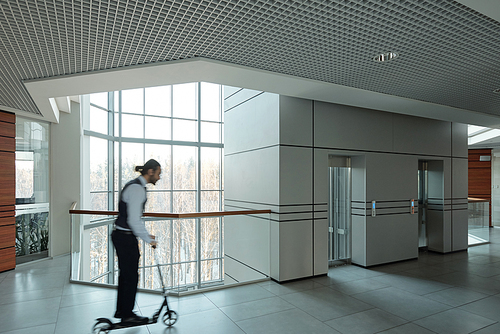 Blurred outline of young businessman moving forwards on scooter inside contemporary business center