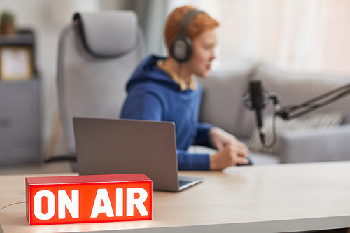 Background image of red ON AIR sign with blurred shape of teenage boy speaking to microphone during online streaming, copy space