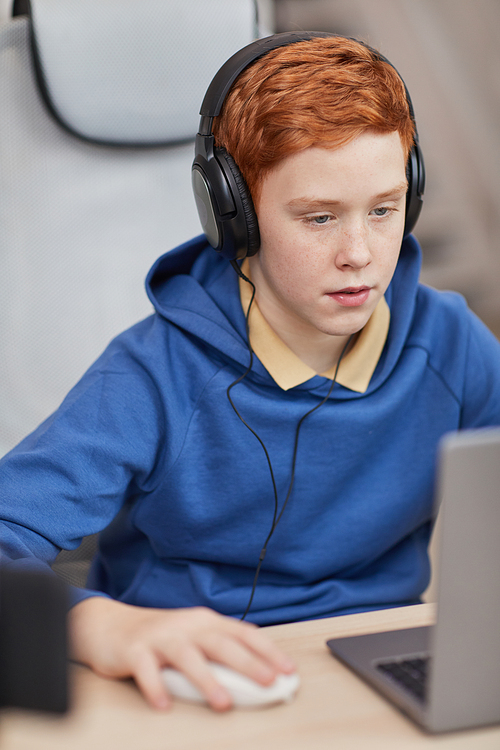Vertical portrait of red haired teenage boy playing video games at home with camera set up for online streaming