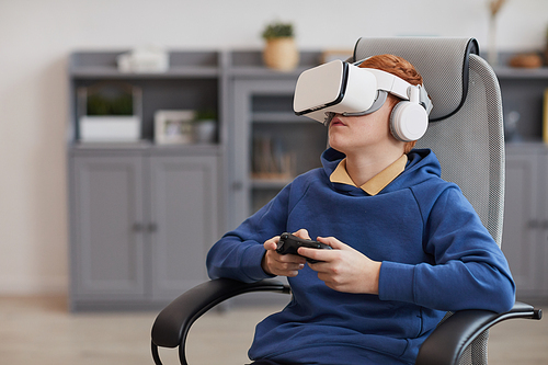 Portrait of teenage boy wearing VR headset and holding gamepad while playing immersive video games, copy space