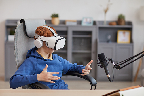 Portrait of teenage boy wearing VR headset and speaking to microphone while playing immersive video games during online streaming, copy space