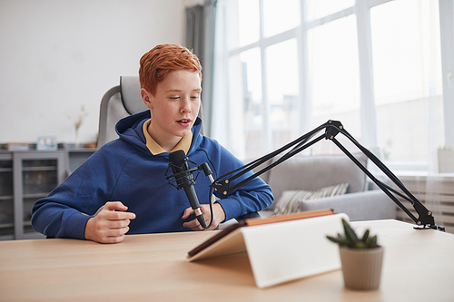 Portrait of red haired teenage boy speaking to microphone an using digital tablet during online lesson or e-learning class, copy space