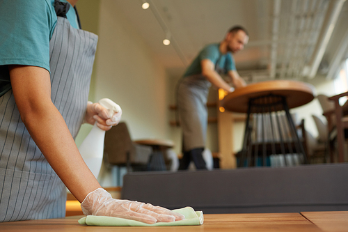 Close up of unrecognizable female waitress cleaning table in coffee shop with warm wooden accents, copy space