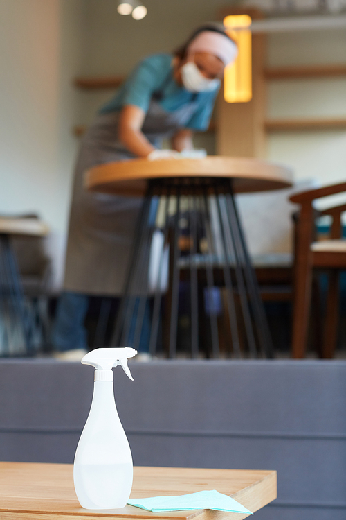 Vertical background image of sanitizing spray bottle on table in cafe with unrecognizable female worker cleaning, copy space