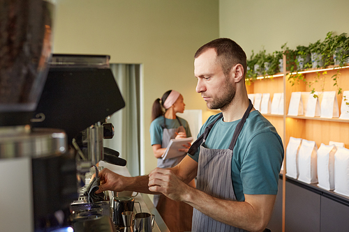 Side view portrait of male barista making fresh coffee in cafe while operating coffee machine, copy space