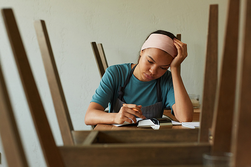 Minimal front view portrait of young African-American woman calculating finances and doing inventory at small business shop, copy space