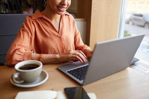 Cropped portrait of smiling young businesswoman using laptop while enjoying work at cafe table, copy space