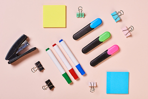 Highlighter pens, whiteboard markers, paper clips and sticker papers on pale pink background, flat lay shot