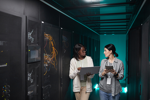 Portrait of two young women using laptop in server room while setting up supercomputer network, copy space