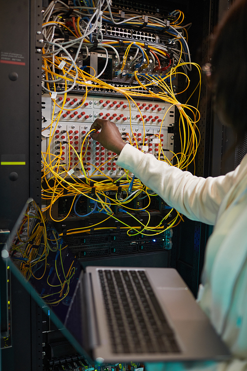 Vertical close up of female network engineer connecting cables in server cabinet while working with supercomputer in data center, copy space