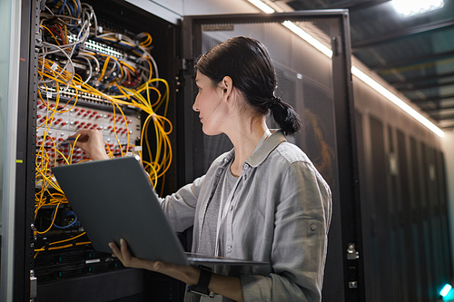 Waist up of female network engineer connecting cables in server cabinet while working with supercomputer in data center, copy space