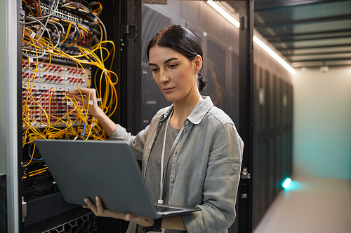 Waist up portrait of female network engineer connecting cables in server cabinet while working with supercomputer in data center, copy space