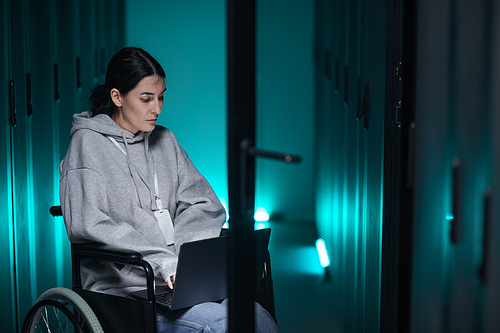 Portrait of disabled woman in wheelchair using laptop while working with supercomputer network in server room, accessible job concept, copy space