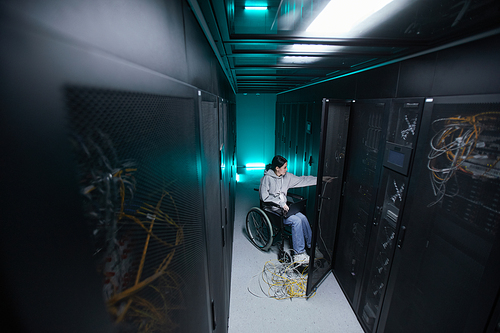 Wide angle portrait of disabled woman in wheelchair working with supercomputer network in server room, accessible job concept, copy space