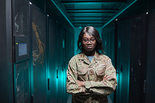 Waist up portrait of tough African-American woman looking at camera while standing in server room with futuristic background, copy space