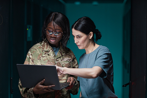Waist up portrait of two women wearing military uniform using laptop while standing in server room, copy space