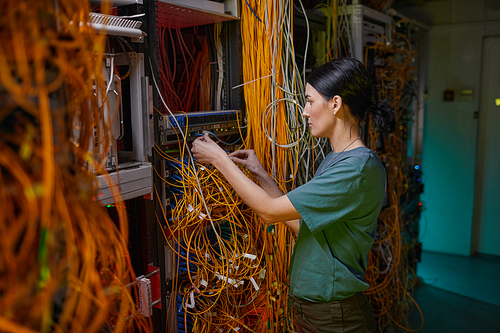 Side view portrait of young woman wearing military uniform inspecting server while working in server room
