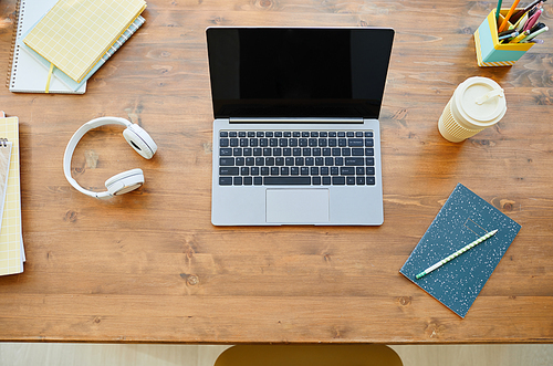 Top down view at teenagers desk with opened laptop on wooden table and accessories, copy space