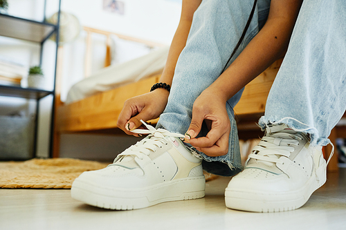 Close up of teenage girl tying shoe laces while sitting on bed ready to go out, copy space