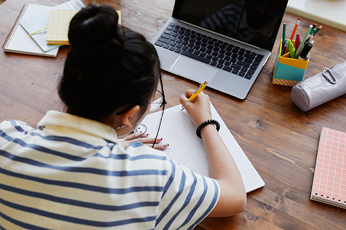 High angle view at teenage girl studying at desk at home and writing in notebook, copy space