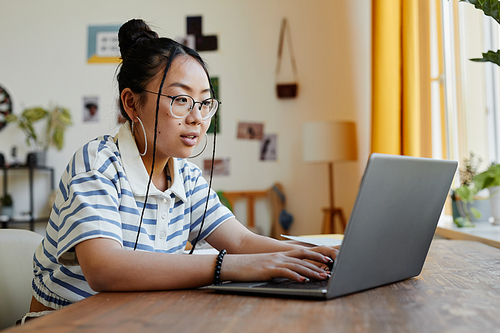 Portrait of Asian teenage girl using laptop while studying at desk at home, copy space