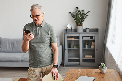 Minimal portrait of modern senior man using smartphone while standing in home interior, copy space