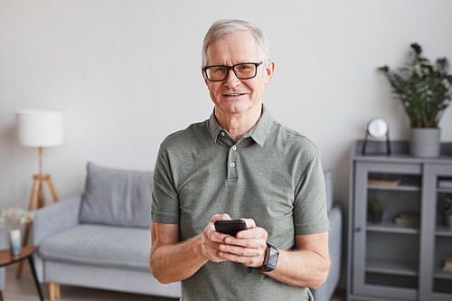 Minimal waist up portrait of smiling senior man using smartphone at home and looking at camera, copy space