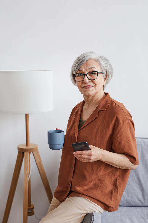 Vertical portrait of modern senior businesswoman looking at camera and enjoying coffee in minimal interior