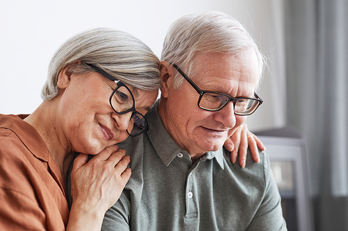 Close up portrait of loving senior couple embracing at home while sitting on couch together and looking at screen, copy space