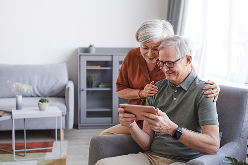 Portrait of happy senior couple using digital tablet together in minimal home interior, copy space