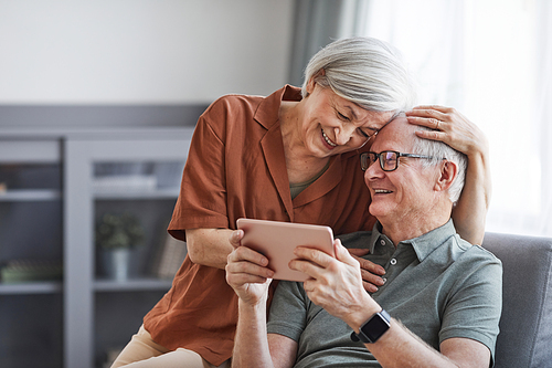 Portrait of happy senior couple using digital tablet together at home and embracing, copy space
