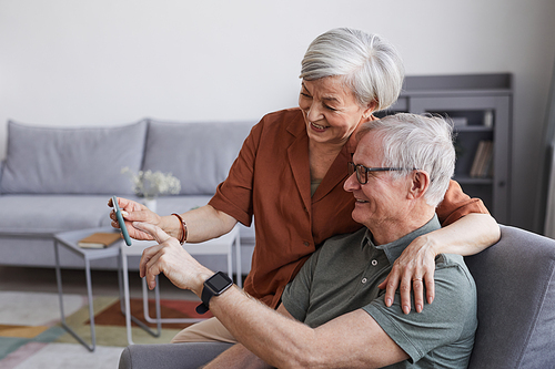 Side view portrait of happy senior couple using smartphone together at home and embracing, copy space