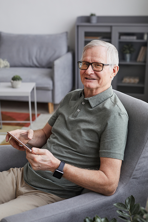Vertical portrait of modern senior man using smartphone at home ans smiling at camera