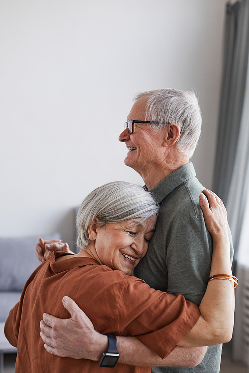 Vertical portrait of loving senior couple dancing at home together in minimal setting, copy space