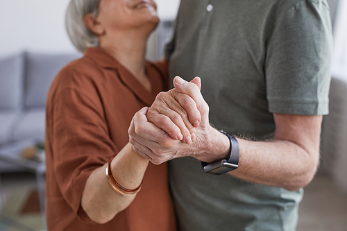 Cropped portrait of loving senior couple dancing at home together and holding hands
