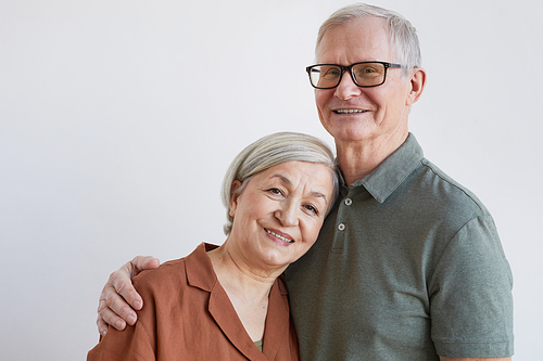 Portrait of happy senior couple embracing and looking at camera while standing against white background, copy space