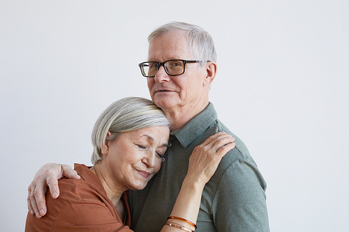 Portrait of loving senior couple embracing and looking at camera while standing against white background, copy space