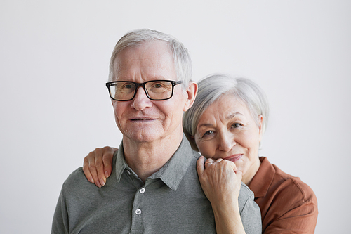Minimal portrait of loving senior couple embracing and looking at camera while standing against white background