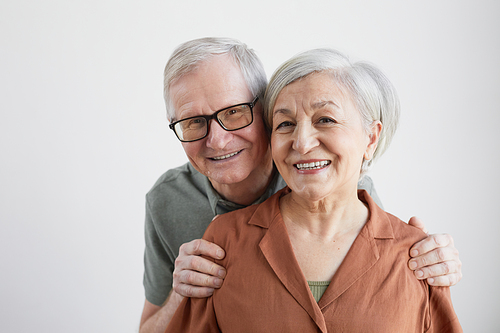 Minimal portrait of happy senior couple embracing husband and looking at camera against white background